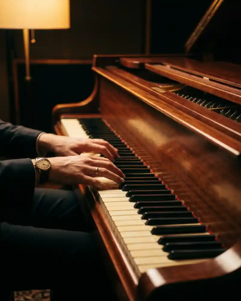 Spotlit hands playing grand piano keys in a dim studio setting